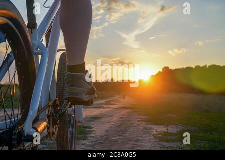 Ein Typ auf einem Mountainbike im roten T-Shirt und mit Rucksack fährt bei Sonnenuntergang auf einer unbefestigten Straße Stockfoto