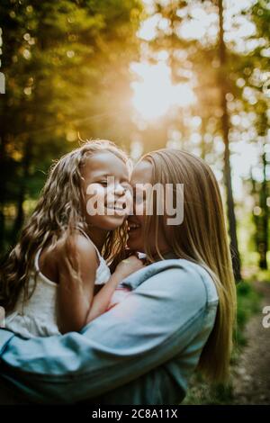 Glückliche Mutter und Tochter lachen und kuscheln im hinterleuchteten Wald Stockfoto