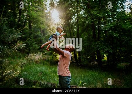 Papa hält Säugling Sohn in der Luft in der Mitten im Wald Stockfoto