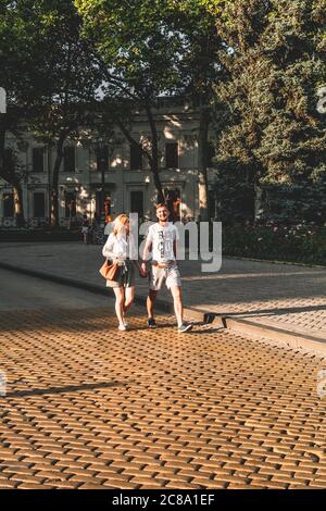 Ukraine, Odessa - 23. August 2019: Ein junges Paar von Liebenden geht vor Sonnenuntergang auf dem Bürgersteig im Odessa Park spazieren. Stockfoto