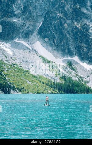 Mann paddeln Boarding auf grünen alpinen See, Granitberg im Rücken Stockfoto