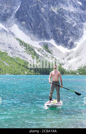 Mann paddeln Boarding auf grünen alpinen See, Granitberg im Rücken Stockfoto