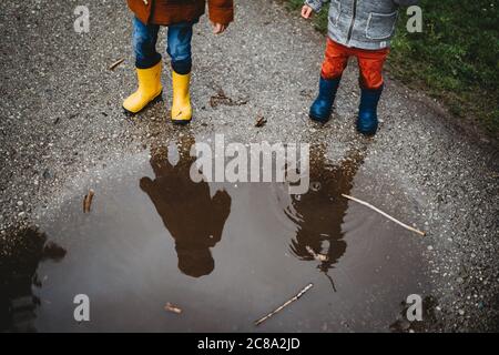 Blick von oben Spiegelung der kleinen Kinder auf Pfütze tragen Regenstiefel Stockfoto