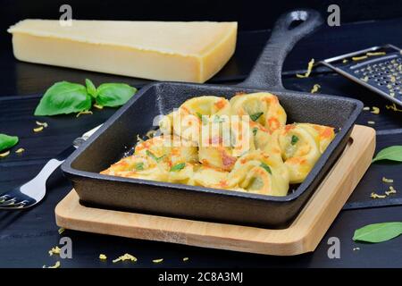 Nahaufnahme von Tortellini mit Parmesan in einer Pfanne auf einem Holzschneidebrett Stockfoto