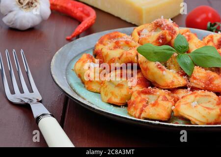 Tortellini mit Tomatensoße und Parmesan in einem Teller auf Holztisch Stockfoto
