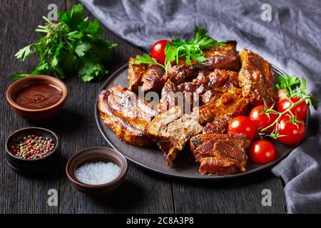 Würzige koreanische geschmorte Schweinefleischrippen - Baek jong Won serviert mit Kirschtomate und Petersilie auf einem schwarzen Teller auf dunklem Holzhintergrund, Nahaufnahme Stockfoto