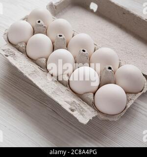 Ungekochte weiße Bio-Eier in einer Papierkiste auf einem weißen Holztisch, Seitenansicht. Nahaufnahme. Stockfoto