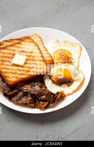 Hausgemachte gesunde Sunnyside Eier Frühstück auf einem weißen Teller auf einer grauen Oberfläche, Seitenansicht. Nahaufnahme. Stockfoto