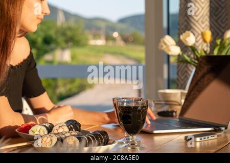 Junge Frau, die von zu Hause aus arbeitet. Freiberufler mit Laptop und das Internet zum Online-Shopping. Glückliches Mädchen lächelt. Arbeitsplatz in gemütlicher Küche Stockfoto