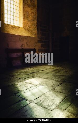 Helles gelbes Licht aus einem mittelalterlichen Fenster erhellt den Steinboden einer romanischen Klosterkirche Stockfoto