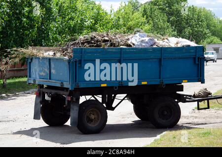 Reinigung von trockenen Ästen und Gras auf Straßen der Stadt Verladung in LKW-Anhänger. Reinigung trocken Blätter Traktor Eimer. Alte Traktoreimer nimmt alte und auf Stockfoto