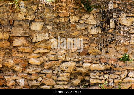 Wand aus Steinen und Ziegelsteinen eines alten Hauses mit kleinen Pflanzen und mit schwarzer Farbe befleckt. Bild für Hintergründe oder Designs Stockfoto