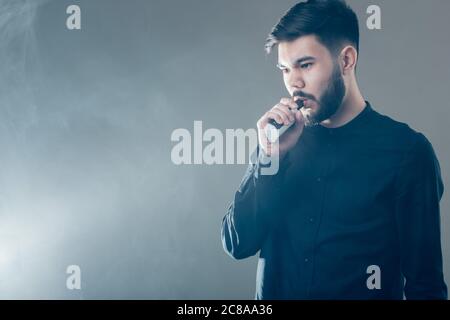 dampfen Mann hält eine mod. Eine Wolke aus Dampf. Schwarzer Hintergrund. Stockfoto