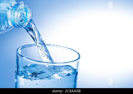 Wasser aus Plastikflasche gegen blauen Gradienten in Glas gießen Stockfoto