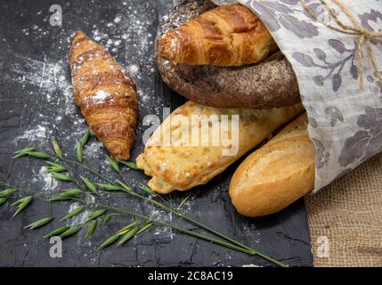 Verschiedene Brotsorten sind in Baumwolltuch und Mehl auf dunklem Schiefergrund verpackt. Stockfoto