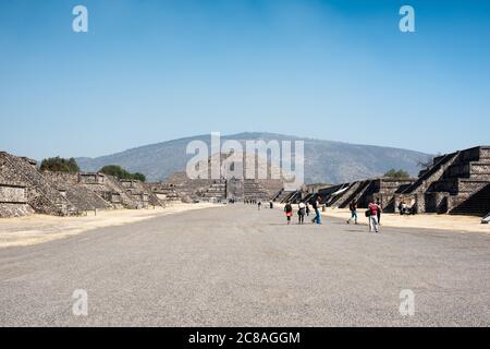 TEOTIHUACAN, Mexiko – Besucher spazieren entlang der Avenue of the Dead, der Hauptdurchgangsstraße der antiken mesoamerikanischen Stadt Teotihuacan. Dieser breite, gerade Boulevard erstreckt sich durch das Herz der archäologischen Stätte und bietet einen beeindruckenden Blick auf die monumentalen Pyramiden und Strukturen, die seinen Weg säumen. Stockfoto