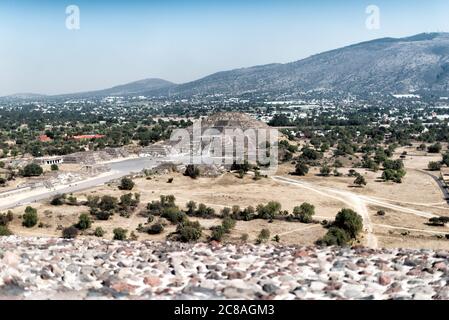 Pyramide der Mondallee der Toten Teotihuacan Mexiko // TEOTIHUACAN, Mexiko — die Pyramide des Mondes von oben auf der Sonnenpyramide an der antiken mesoamerikanischen archäologischen Stätte Teotihuacan. Die Avenue of the Dead, die Hauptdurchgangsstraße dieser präkolumbischen Stadt, erstreckt sich zwischen diesen beiden großen Pyramidenbauten. Teotihuacan blühte zwischen etwa 100 und 650 n. Chr. und gehörte mit einer Bevölkerung von über 100.000 Menschen zu den größten Städten der Antike. Die Pyramide des Mondes, die etwa 43 Meter (141 Fuß) hoch ist, verankert das NO Stockfoto