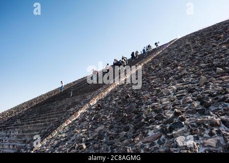 Pyramide der Sonne Besucher Teotihuacan Mexiko // TEOTIHUACAN, Mexiko — Besucher klettern die steilen Stufen der Pyramide der Sonne an der archäologischen Stätte Teotihuacan. Dieses monumentale Gebäude, eine der größten antiken Pyramiden Amerikas, erhebt sich etwa 216 Fuß (66 Meter) hoch und misst etwa 720 Fuß (220 Meter) an seiner Basis. Die Pyramide wurde um 100-450 n. Chr. von der antiken Teotihuacan-Zivilisation errichtet, deren Identität den Archäologen weitgehend unbekannt ist. Teotihuacan war eine der größten Städte in der Antike, mit einer Bevölkerung von bis zu zehn Stockfoto