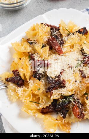 Pasta mit sonnengetrockneten Tomaten und Parmesan auf einem weißen Teller auf dem Tisch. Italienisches Gericht, vertikales Bild Stockfoto