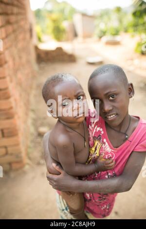 Joan Nkinzi (10) trägt ihren kleinen Bruder Luice Ssekalala (12 Monate) zu sich nach Hause im Masaka District, Uganda. Beide sind Kinder von VEA James Kabiito Stockfoto