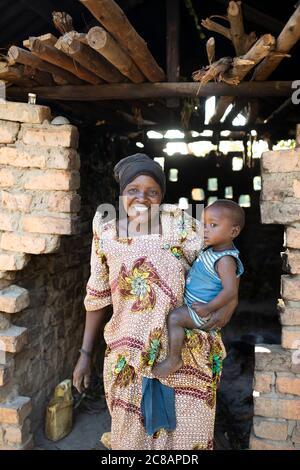 Porträt einer afrikanischen Mutter in einem traditionellen ugandischen Gomesi-Kleid, während sie ihr Kind in der Tür ihrer Hütte in Lyantondo, Uganda, hält. Stockfoto