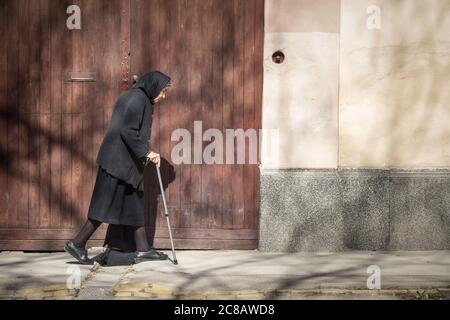 SOMBOR, SERBIEN - 19. MÄRZ 2016: Alte Frau mit einem traditionellen Rückenkostüm, die alleine in den Straßen von Sombor geht. Die serbische Gesellschaft ist curr Stockfoto