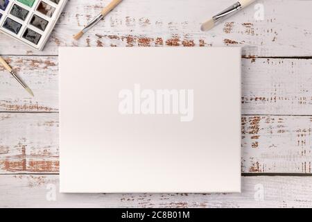 Aquarellfarben, Pinsel und weiße Leinwand auf weißem, hölzernen Schreibtisch. Speicherplatz kopieren. Draufsicht. Stockfoto