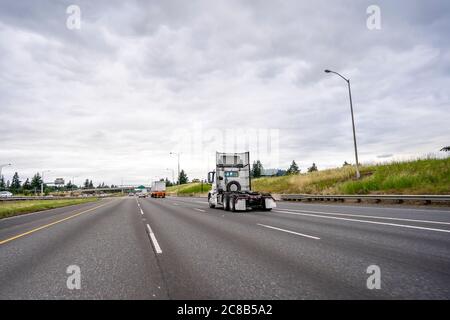 Big Rig weiß glänzend Industrie Diesel High Cab leistungsstarke Sattelzugmaschine ohne Sattelauflieger läuft auf der breiten mehrzeiligen Autobahn Straße hinter o Stockfoto