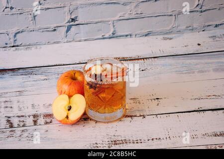 Ein tiefes Kristallglas aus Apfelwein mit Zimt und Anis steht auf einem Holztisch, neben einem halben und einem ganzen roten Apfel. Nahaufnahme. Stockfoto