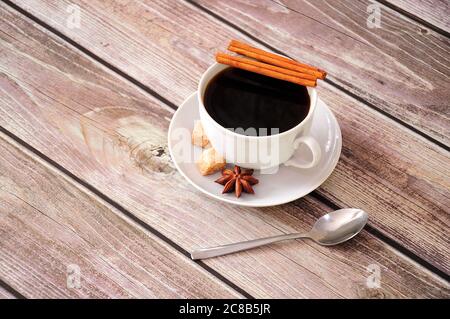 Auf einer Untertasse auf einem Holztisch steht eine Tasse schwarzen Kaffee mit Zimtanis und Scheiben braunem Rohrzucker. Nahaufnahme. Stockfoto