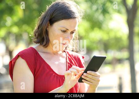 Seriöse Erwachsene Frau mit Smartphone in einem Park einen sonnigen Tag stehen Stockfoto
