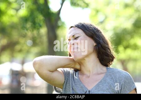 Frau mittleren Alters in Schmerzen leiden Nackenschmerzen stehen in einem Park im Sommer Stockfoto