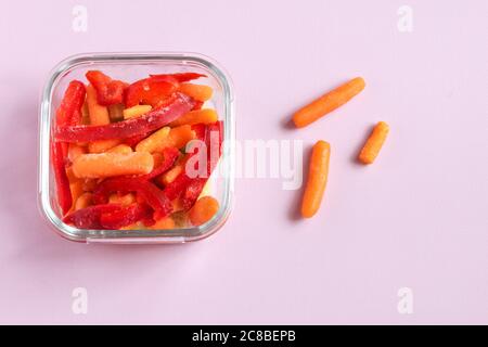 Gefrorenes Gemüse wie roter Paprika und Baby Karotte in den transparenten Schalen auf dem rosa Hintergrund mit Copyspace. Draufsicht. Stockfoto