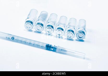 Spritze und Reihe von Glasfläschchen mit Medikamenten auf weißem Hintergrund. Blauton. Stockfoto