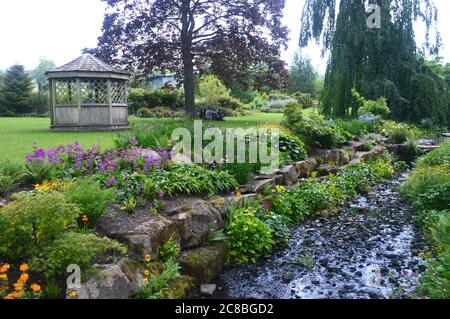 Das Beck Flowing by Wooden Summerhouse im RHS Garden Harlow Carr, Harrogate, Yorkshire, England, Großbritannien. Stockfoto