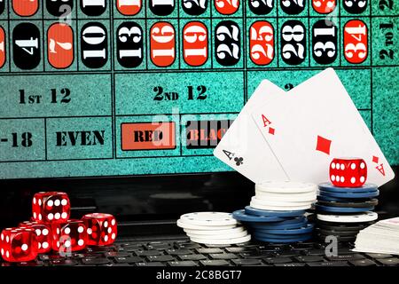 Würfel, Spielkarten und Chips auf Laptop mit Roulette-Tisch auf dem Bildschirm, Online-Glücksspiel-Konzept Stockfoto