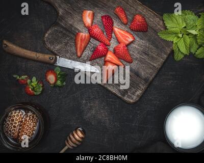 Holzkiste mit frischen Erdbeeren, einer Tasse Honig, einer Tasse Milch und einem Teller Minzblätter auf dem Vintage-Tisch. Overhead-Aufnahme mit Kopierplatz. Stockfoto