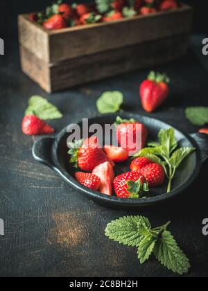 Holzkiste mit frischen Erdbeeren und schwarzer Schale Erdbeeren auf Vintage-Tisch. Stockfoto