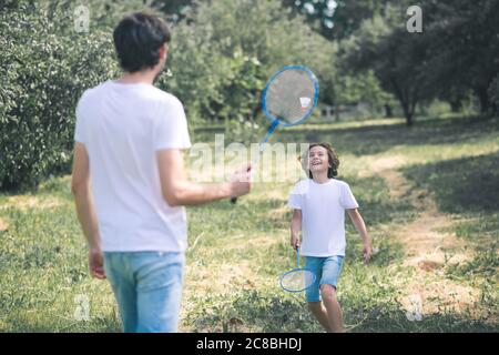 Dunkelhaariger Junge und sein Vater spielen Badminton im Park Stockfoto