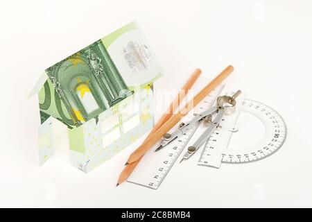 Haus in Euro-Banknoten mit Bleistiften, Linealen und Kompassen auf Weiß eingewickelt Stockfoto