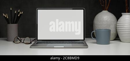 Nahaufnahme des Arbeitsbereichs mit Laptop, Bleistiften, Gläsern und Keramikvasen auf weißem Tisch, Schneideweg. Stockfoto