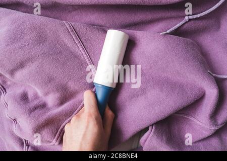 Hände mit blauer Haftwalze zum Reinigen von Kleidung. Nahaufnahme Stockfoto