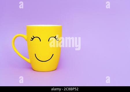 Gelbe Kaffeetasse mit Smiley auf violettem Hintergrund. Happy friday Wort Konzept. Minimalismus Stil, romantische Stimmung, guten Morgen, Glück, Pause. Stockfoto