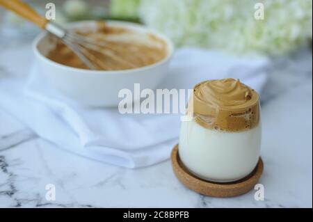 Iced Dalgona Coffee, ein trendiger, flauschiger, cremiger Kaffee mit einer Schüssel Sahne und Whisker. Geschmolzener Kaffee mit Sahne verrühren Stockfoto