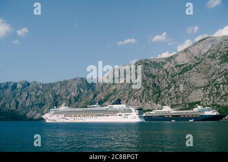 Zwei riesige Kreuzfahrtschiffe in der Bucht von Kotor in Montenegro, vor dem Hintergrund von felsigen Bergen und blauem Himmel. In der Nähe der Städte Dobrota und Ljuta. Stockfoto