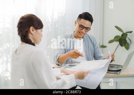 Immobilienmakler zeigt ein Bauprojekt auf einem digitalen Tablet zu jungen asiatischen Mann. Stockfoto