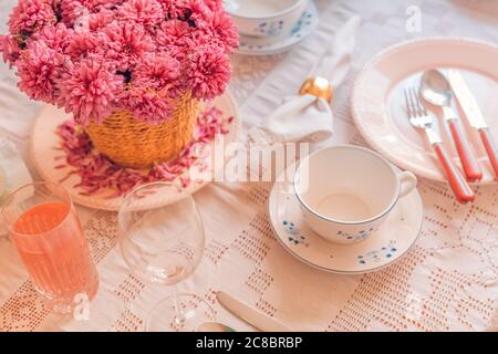 Festliche Tischeinrichtung in pastellfarbenen Tellern und Besteck. Elegante Dinner-Party mit Blumen- und Weingläsern, Tageslicht Stockfoto
