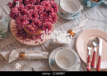 Festliche Tischeinrichtung in pastellfarbenen Tellern und Besteck. Elegante Dinner-Party mit Blumen- und Weingläsern, Tageslicht Stockfoto