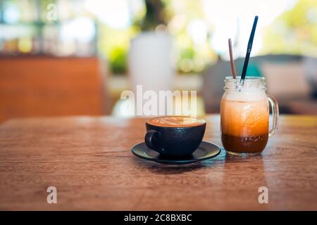 Gläser mit Eiskaffee Latte Art auf Holztischplatte. Natürliches Licht, morgens entspannende Stimmung, beginnen Sie den Tag mit Kaffee, verschwommenem Sonnenlicht, Natur Stockfoto