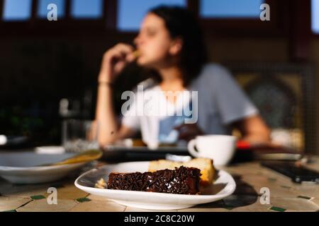Selektive Fokussierung auf einen Teller mit Schokoladenkuchen, wobei eine Frau im Hintergrund in einem Holzrestaurant in Marokko außer Fokus isst Stockfoto